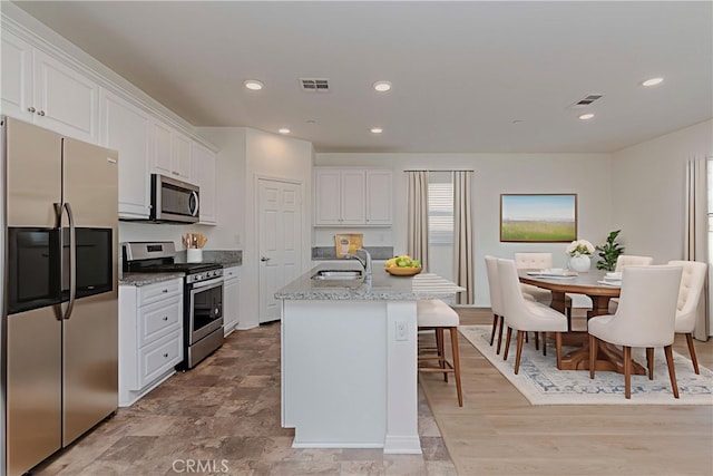 24679 Acadia Dr, Corona, CA 92883 - kitchen featuring appliances with stainless steel finishes, white cabinetry, a kitchen island with sink, a breakfast bar area, and recessed lighting