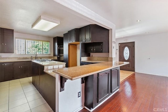 347 E 97th St, Los Angeles, CA 90003 - kitchen with light countertops, oven, a peninsula, dark brown cabinetry, and a breakfast bar area