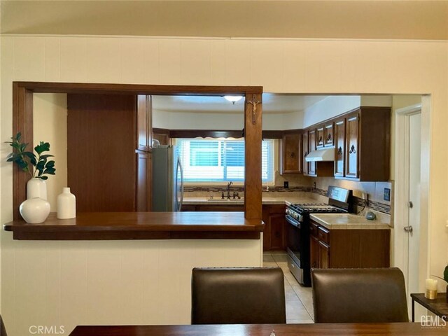 2720 Baylor St, Bakersfield, CA 93305 - kitchen with gas range, under cabinet range hood, freestanding refrigerator, dark brown cabinets, and a peninsula