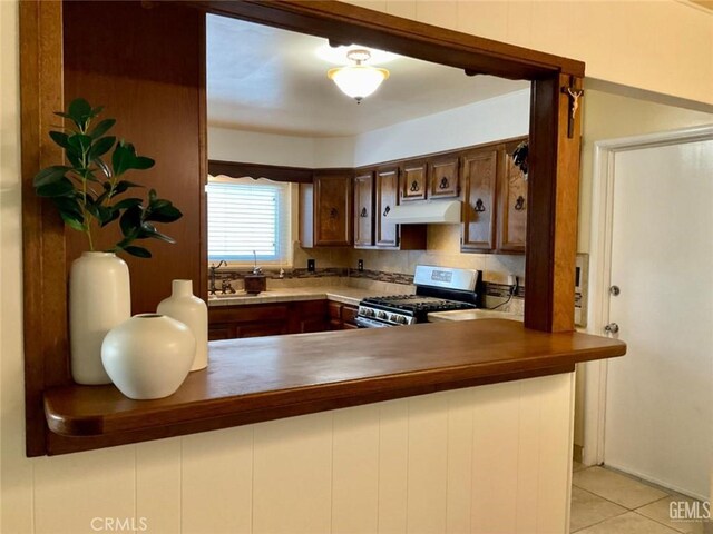 2720 Baylor St, Bakersfield, CA 93305 - kitchen featuring stainless steel gas range, under cabinet range hood, a peninsula, and light tile patterned flooring