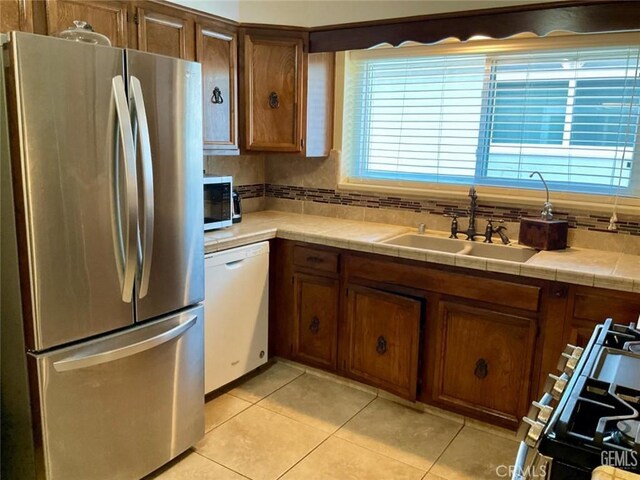 2720 Baylor St, Bakersfield, CA 93305 - kitchen with stainless steel appliances, light tile patterned floors, tile counters, brown cabinets, and tasteful backsplash