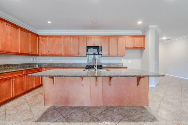 26946 Shelter Cove Ct, Menifee, CA 92585 - kitchen featuring black microwave, ornamental molding, dark stone counters, a breakfast bar, and an island with sink