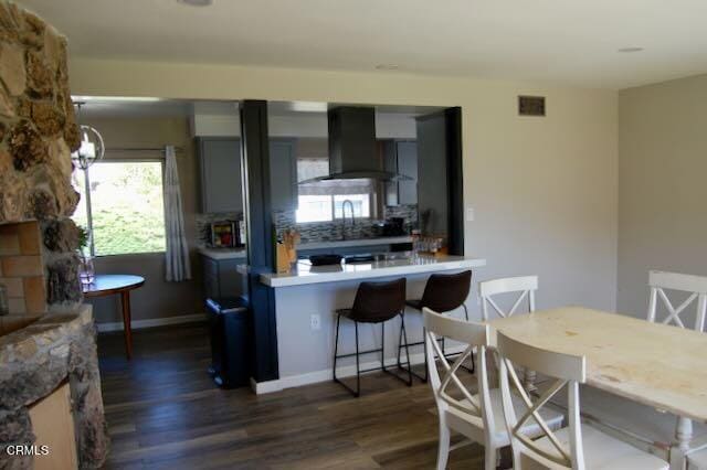 691 Via Ondulando, Ventura, CA 93003 - kitchen featuring wall chimney range hood, dark wood-style floors, tasteful backsplash, light countertops, and a breakfast bar
