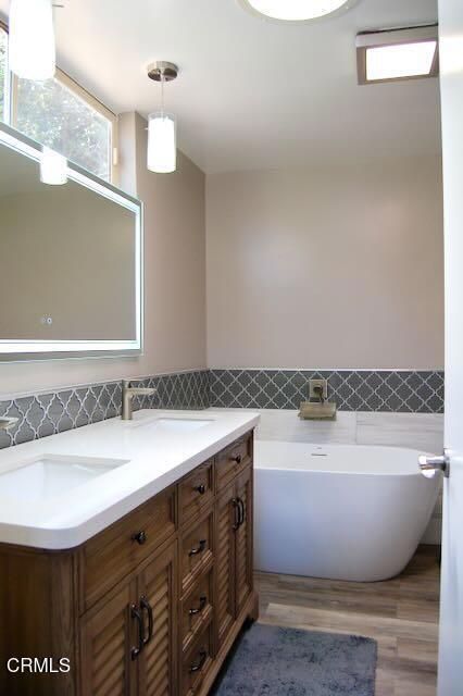 691 Via Ondulando, Ventura, CA 93003 - full bathroom with a freestanding bath, double vanity, tile walls, wood finished floors, and wainscoting