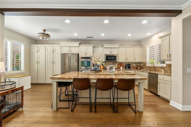 14131 Apple Grove Ct, Eastvale, CA 92880 - kitchen featuring appliances with stainless steel finishes, a center island, light wood finished floors, tasteful backsplash, and a kitchen bar