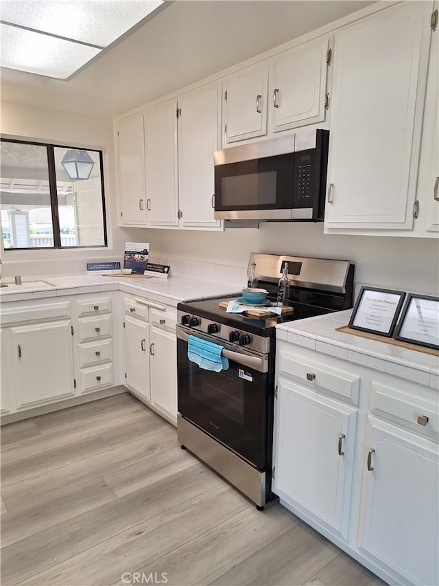 3144 Via Vis Unit Q, Laguna Woods, CA 92637 - kitchen with appliances with stainless steel finishes, tile countertops, white cabinets, and light wood-style flooring