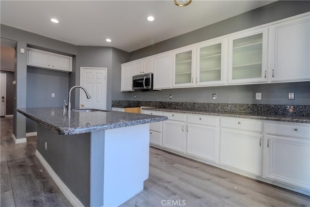 13740 Starshine Dr, Victorville, CA 92392 - kitchen featuring stainless steel microwave, dark stone counters, light wood-type flooring, white cabinets, and glass insert cabinets