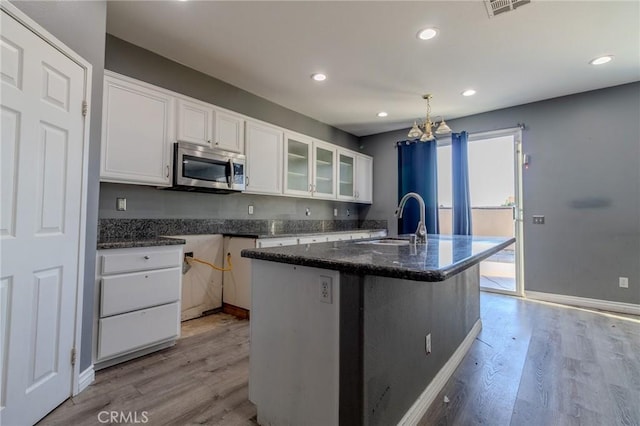 13740 Starshine Dr, Victorville, CA 92392 - kitchen with stainless steel microwave, white cabinets, light wood-style floors, glass insert cabinets, and dark stone counters