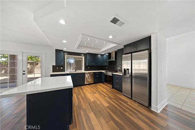 40132 White Leaf Ln, Murrieta, CA 92562 - kitchen with appliances with stainless steel finishes, wall chimney exhaust hood, a tray ceiling, light countertops, and tasteful backsplash