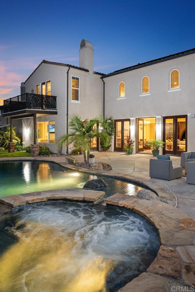 7603 Circulo Sequoia, Carlsbad, CA 92009 - back of house at dusk with stucco siding, a patio area, a balcony, a chimney, and a pool with connected hot tub