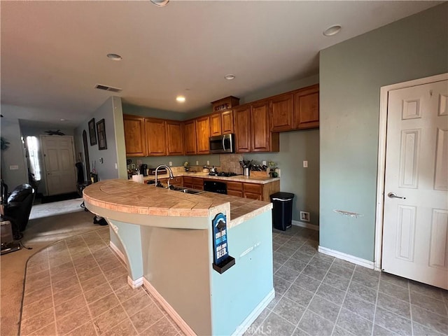6227 Ocean Jasper Dr, Bakersfield, CA 93313 - kitchen featuring stainless steel microwave, brown cabinets, tile countertops, black gas stovetop, and a center island with sink