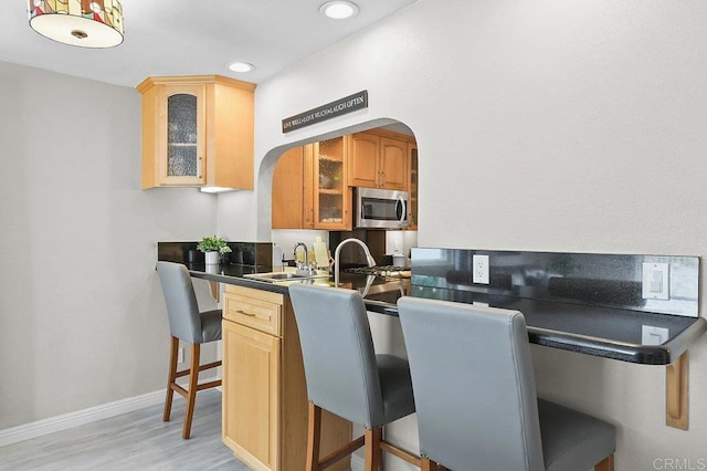 9933 Golden W Ln, Santee, CA 92071 - kitchen featuring stainless steel microwave, a breakfast bar area, dark countertops, glass insert cabinets, and light wood finished floors