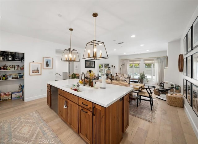1212 Carmel St, San Luis Obispo, CA 93401 - kitchen featuring brown cabinetry, light wood-style floors, light countertops, a center island with sink, and decorative light fixtures