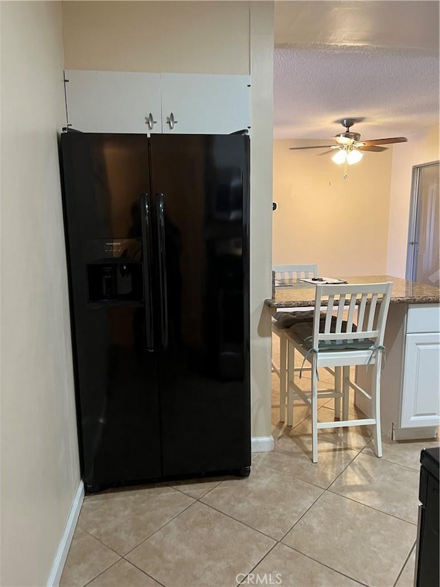 1441 Edgewood Ln, Hemet, CA 92543 - kitchen featuring black fridge with ice dispenser, light tile patterned floors, ceiling fan, white cabinetry, and stone countertops
