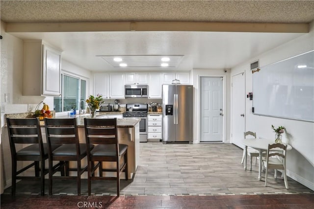 6073 Cameo St, Rancho Cucamonga, CA 91701 - kitchen featuring stainless steel appliances, a peninsula, white cabinetry, a kitchen breakfast bar, and light wood-style flooring