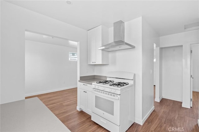 715 N 3rd St, Lompoc, CA 93436 - kitchen with white gas range oven, wall chimney exhaust hood, white cabinets, and wood finished floors