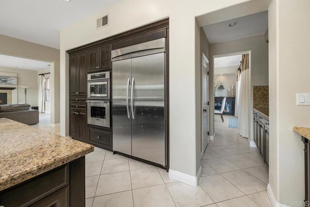 13388 Greenstone Ct, Scripps Miramar, CA 92131 - kitchen with appliances with stainless steel finishes, dark brown cabinetry, light tile patterned flooring, light stone counters, and decorative backsplash