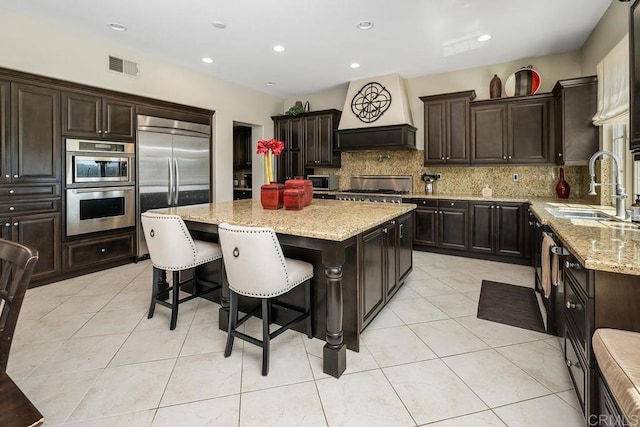 13388 Greenstone Ct, Scripps Miramar, CA 92131 - kitchen featuring stainless steel appliances, a center island, premium range hood, tasteful backsplash, and light stone countertops