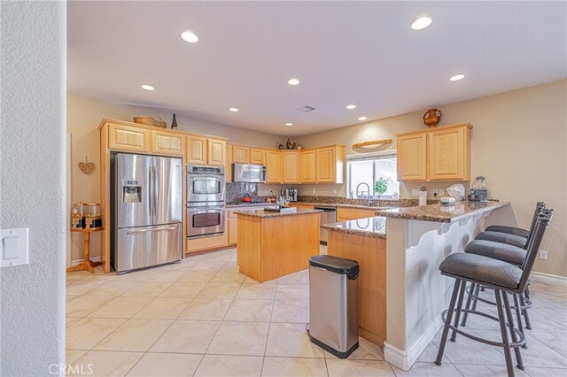 2534 Desert Rose Dr, Lancaster, CA 93536 - kitchen with appliances with stainless steel finishes, light brown cabinets, light stone countertops, recessed lighting, and a center island