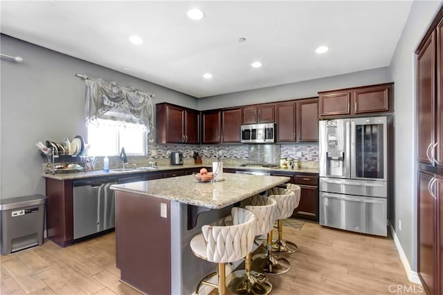 26810 Sugarite Canyon Dr, Moreno Valley, CA 92555 - kitchen featuring appliances with stainless steel finishes, light wood finished floors, a kitchen island, tasteful backsplash, and light stone countertops