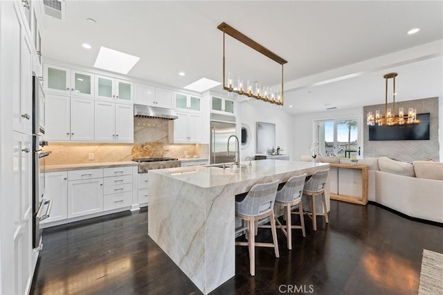 444 Morning Canyon Rd, Corona Del Mar, CA 92625 - kitchen featuring under cabinet range hood, light stone countertops, dark wood-style flooring, white cabinetry, and decorative backsplash