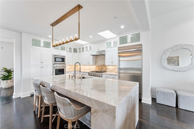 444 Morning Canyon Rd, Corona Del Mar, CA 92625 - kitchen featuring built in appliances, under cabinet range hood, a skylight, white cabinets, and a large island