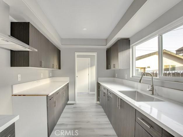 1438 W 69th St, Los Angeles, CA 90047 - kitchen with custom exhaust hood, light countertops, light wood-style flooring, gray cabinetry, and modern cabinets