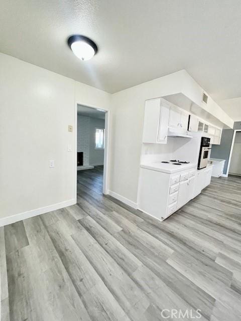 28838 Snead Dr, Menifee, CA 92586 - kitchen featuring light wood-type flooring, white cabinets, light countertops, oven, and under cabinet range hood