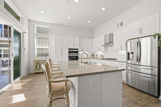 2035 Bravo Loop Unit 6, Chula Vista, CA 91915 - kitchen with stainless steel appliances, wall chimney range hood, light wood finished floors, a kitchen island with sink, and white cabinets