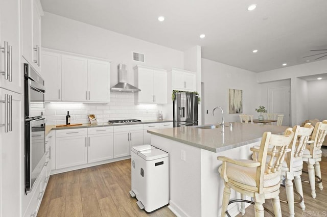 2035 Bravo Loop Unit 6, Chula Vista, CA 91915 - kitchen with appliances with stainless steel finishes, wall chimney range hood, light wood-style floors, a kitchen island with sink, and backsplash