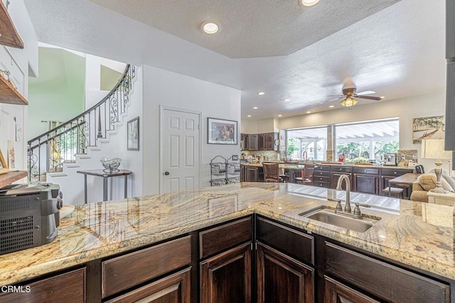 4665 Northridge Dr, Palmdale, CA 93551 - kitchen with a ceiling fan, dark brown cabinetry, light stone countertops, a textured ceiling, and open floor plan