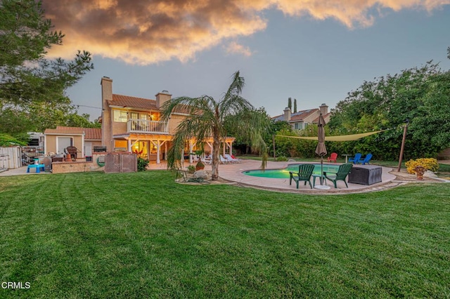 4665 Northridge Dr, Palmdale, CA 93551 - back of house at dusk with a balcony, a patio area, a yard, a chimney, and stucco siding