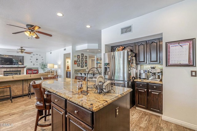 4665 Northridge Dr, Palmdale, CA 93551 - kitchen featuring ceiling fan, light wood-style flooring, dark brown cabinetry, a kitchen island, and light stone countertops