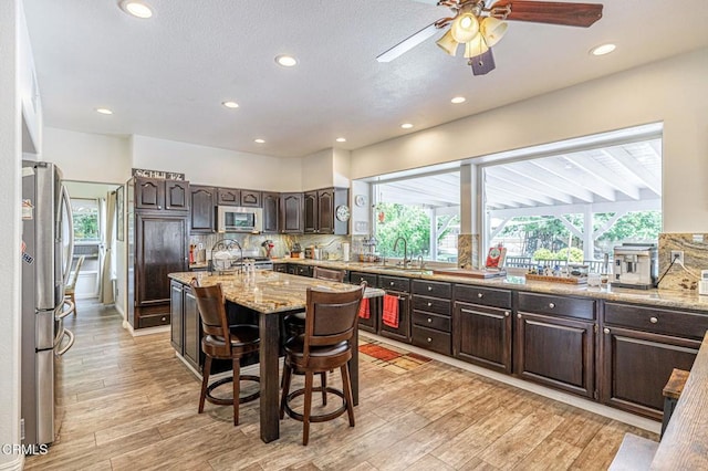 4665 Northridge Dr, Palmdale, CA 93551 - kitchen with stainless steel appliances, dark brown cabinetry, tasteful backsplash, a center island, and ceiling fan
