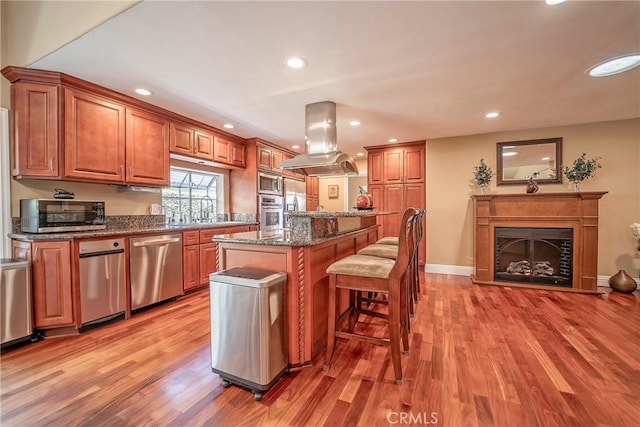 25532 Maximus St, Mission Viejo, CA 92675 - kitchen featuring appliances with stainless steel finishes, island range hood, a kitchen bar, light wood finished floors, and brown cabinetry