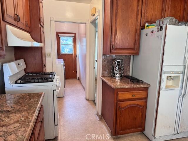 15945 Lashburn St, Whittier, CA 90603 - kitchen with white appliances, under cabinet range hood, brown cabinets, washer / dryer, and backsplash