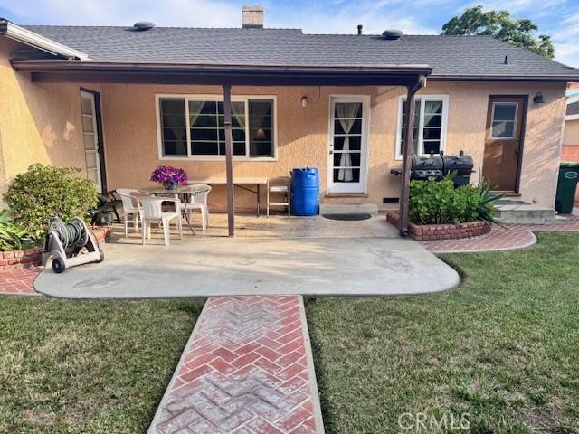 15945 Lashburn St, Whittier, CA 90603 - rear view of property featuring a patio, stucco siding, a lawn, a shingled roof, and a chimney