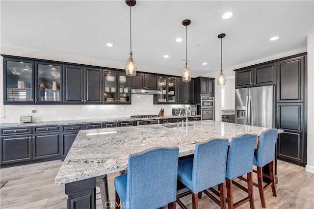 33303 Barmetta Ln, Temecula, CA 92592 - kitchen with stainless steel appliances, under cabinet range hood, backsplash, light wood finished floors, and a breakfast bar area