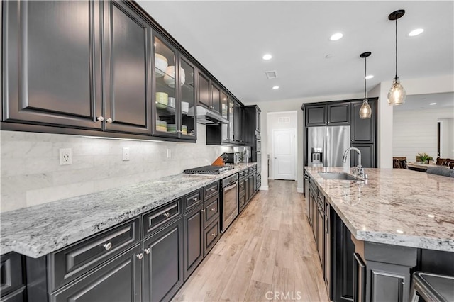 33303 Barmetta Ln, Temecula, CA 92592 - kitchen with backsplash, light wood-style floors, light stone countertops, appliances with stainless steel finishes, and a kitchen island with sink