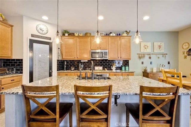 44837 Checkerbloom Dr, Temecula, CA 92592 - kitchen featuring stainless steel microwave, backsplash, decorative light fixtures, a breakfast bar, and an island with sink