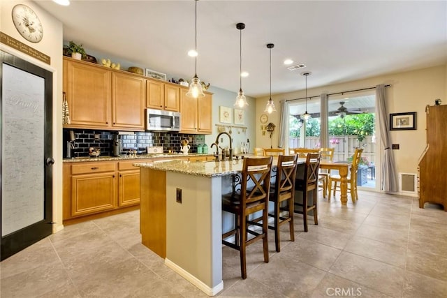 44837 Checkerbloom Dr, Temecula, CA 92592 - kitchen featuring stainless steel microwave, decorative backsplash, light stone countertops, a kitchen breakfast bar, and an island with sink