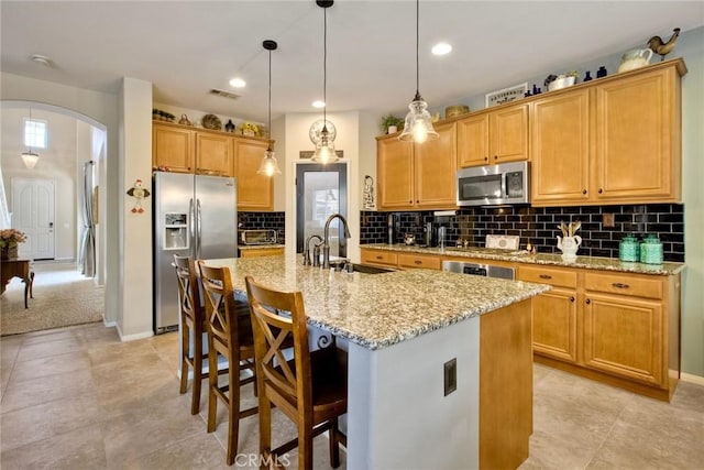 44837 Checkerbloom Dr, Temecula, CA 92592 - kitchen with appliances with stainless steel finishes, arched walkways, a center island with sink, light stone countertops, and a kitchen breakfast bar
