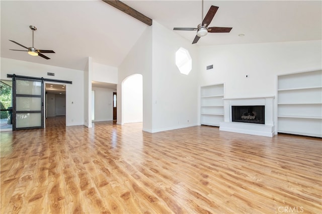 9411 Friendly Woods Ln, Whittier, CA 90605 - unfurnished living room with high vaulted ceiling, a ceiling fan, built in shelves, a barn door, and a fireplace with raised hearth