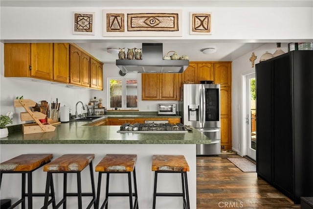 2023 Republic Ave, Costa Mesa, CA 92627 - kitchen with stainless steel appliances, wall chimney range hood, a peninsula, brown cabinetry, and dark countertops
