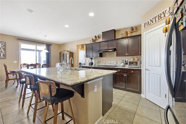 863 Legacy Dr, Lemoore, CA 93245 - kitchen with freestanding refrigerator, a center island with sink, a breakfast bar area, light stone countertops, and under cabinet range hood