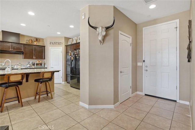 863 Legacy Dr, Lemoore, CA 93245 - kitchen with a breakfast bar, dark brown cabinets, black refrigerator with ice dispenser, light tile patterned flooring, and recessed lighting