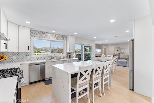 3208 Calle Grande, San Clemente, CA 92672 - kitchen with stainless steel appliances, light wood-type flooring, tasteful backsplash, white cabinets, and a breakfast bar