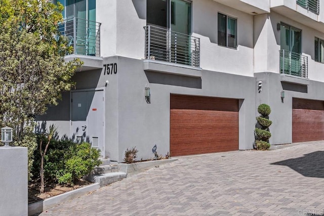 7570 Gibraltar St Unit 101, Carlsbad, CA 92009 - view of front of house with stucco siding, a garage, decorative driveway, and a balcony