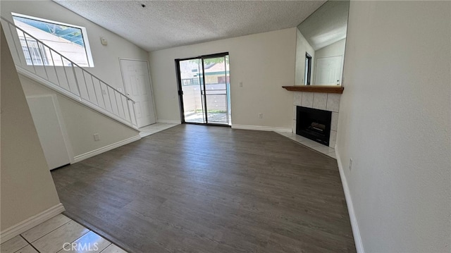 44460 15th St E Unit 13, Lancaster, CA 93535 - unfurnished living room with vaulted ceiling, stairway, a tiled fireplace, a textured ceiling, and wood finished floors
