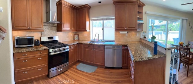2690 Peralta Ct, Tustin, CA 92782 - kitchen featuring stainless steel appliances, wall chimney exhaust hood, a peninsula, light wood-type flooring, and dark stone counters
